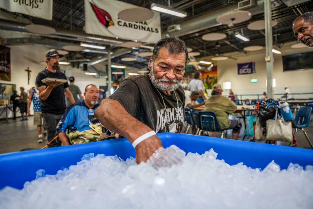 A man experiencing homelessness grabbing a bottle of water from the distribution bucket.